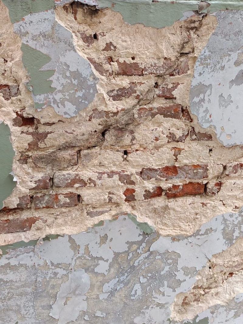 Pared deteriorada antes del trabajo: revoque desprendido, ladrillos a la vista y pintura verde descascarada.