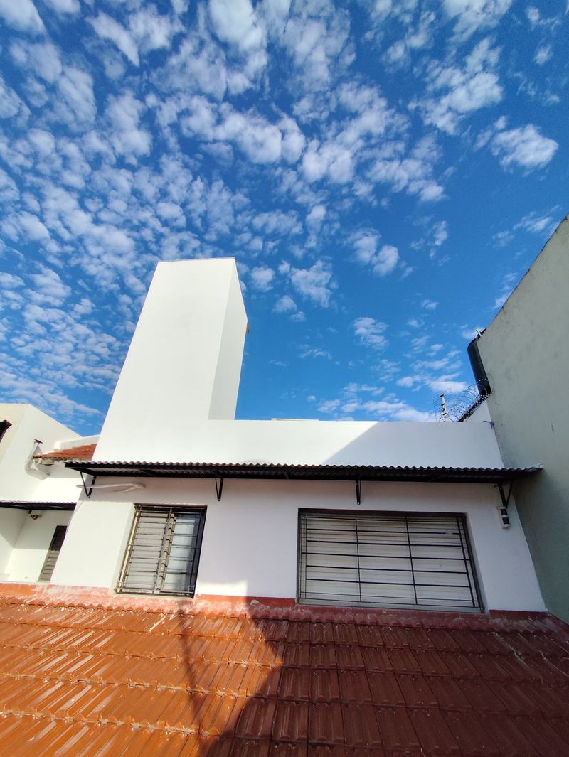 La misma terraza terminada: paredes y torre del tanque revocadas y pintadas de blanco, con techo de tejas y cielo azul.