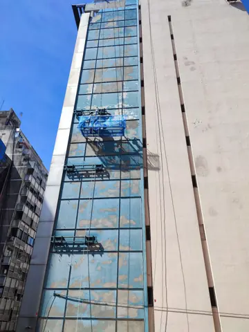 Fachada de edificio alto con operario trabajando en altura.