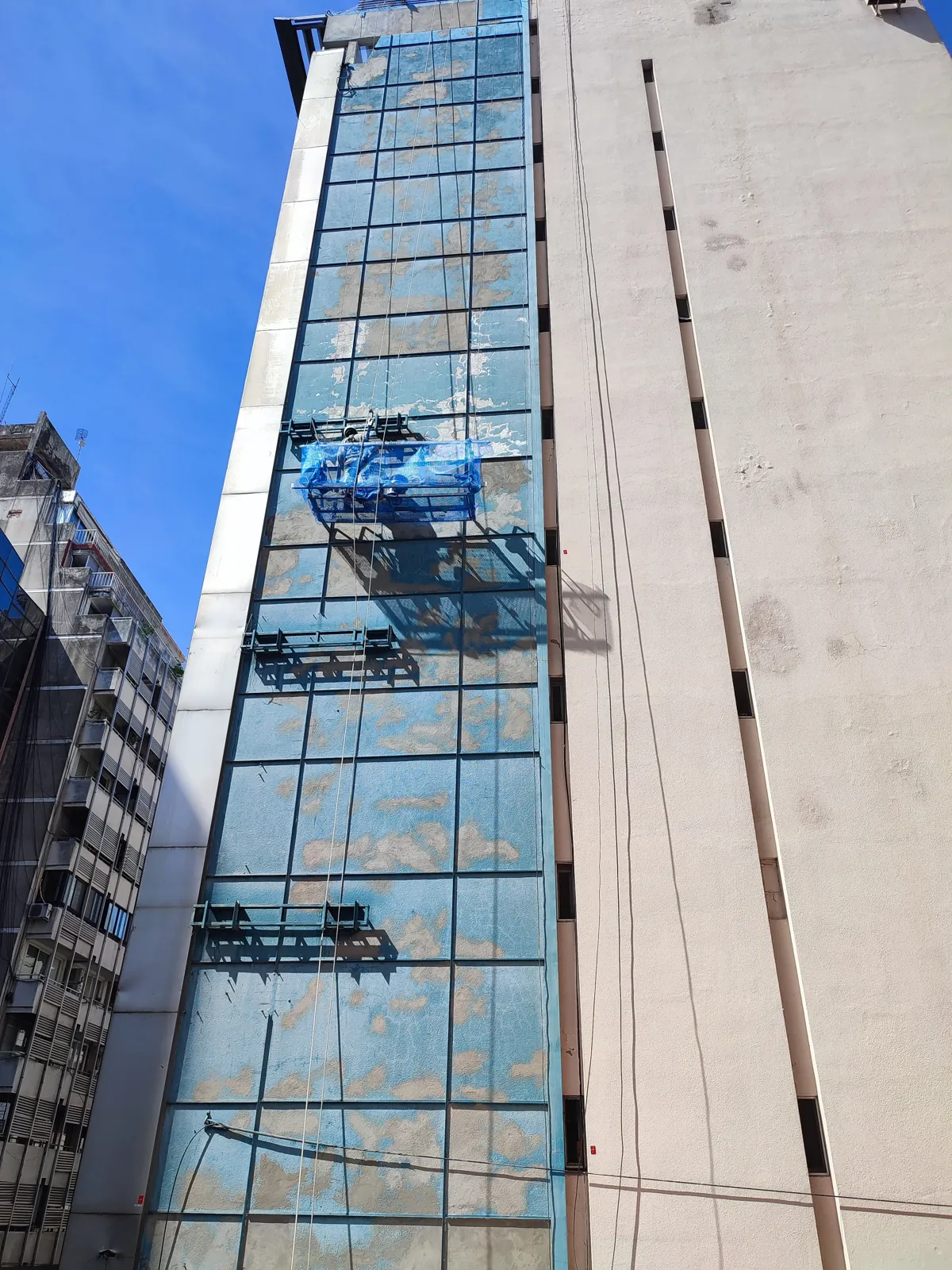 Fachada de edificio alto con operario trabajando en altura.