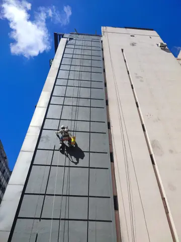 Operario colgado trabajando en la fachada de un edificio alto.
