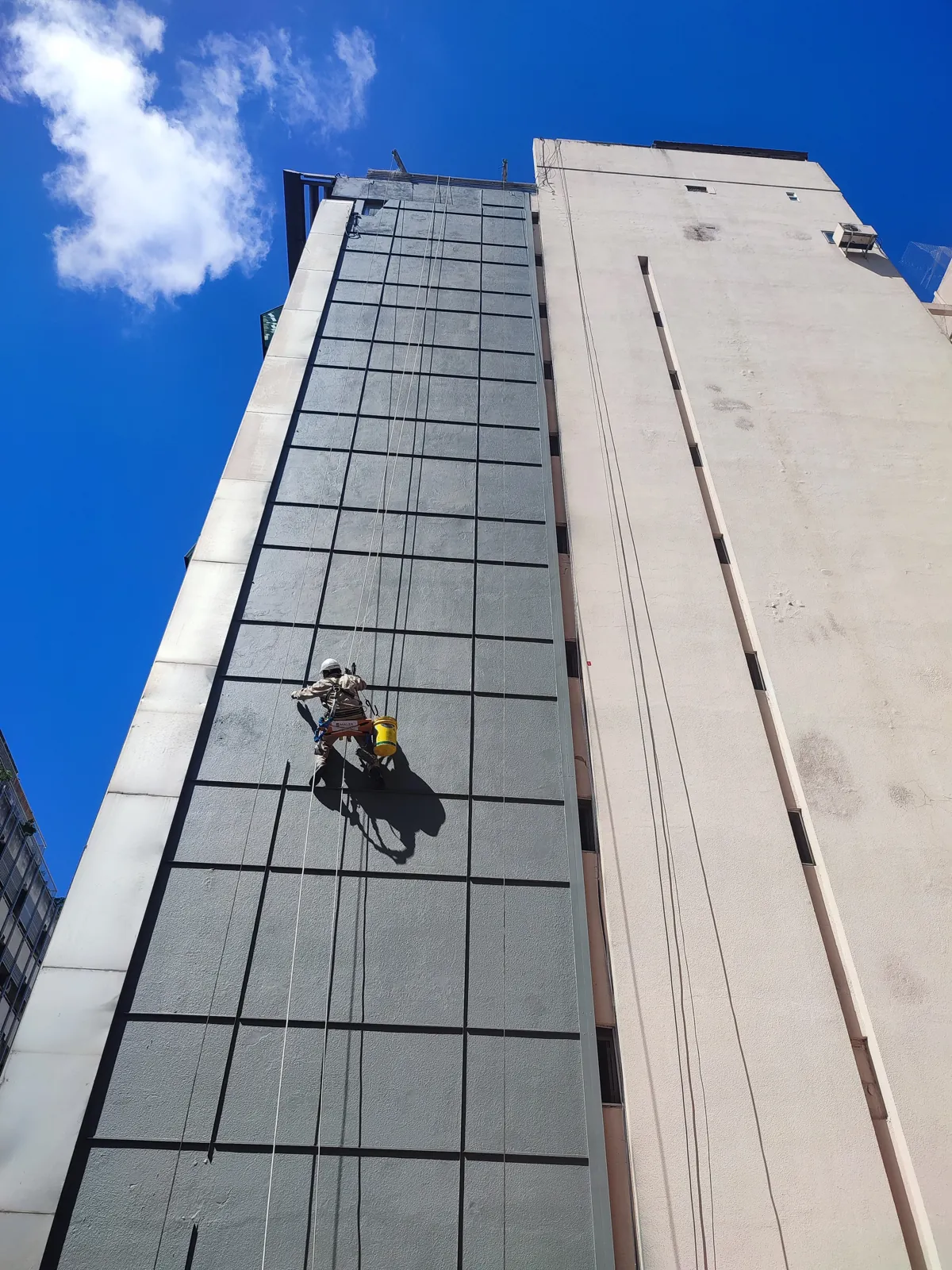Operario colgado trabajando en la fachada de un edificio alto.