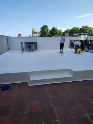 Operarios aplicando membrana blanca en una terraza.