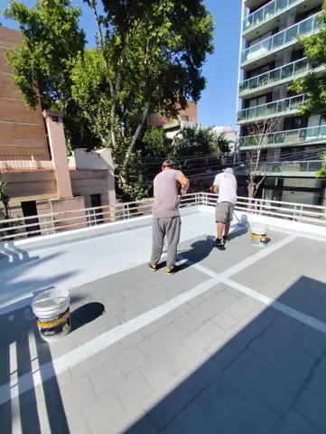 Operarios aplicando membrana en la terraza de un edificio.
