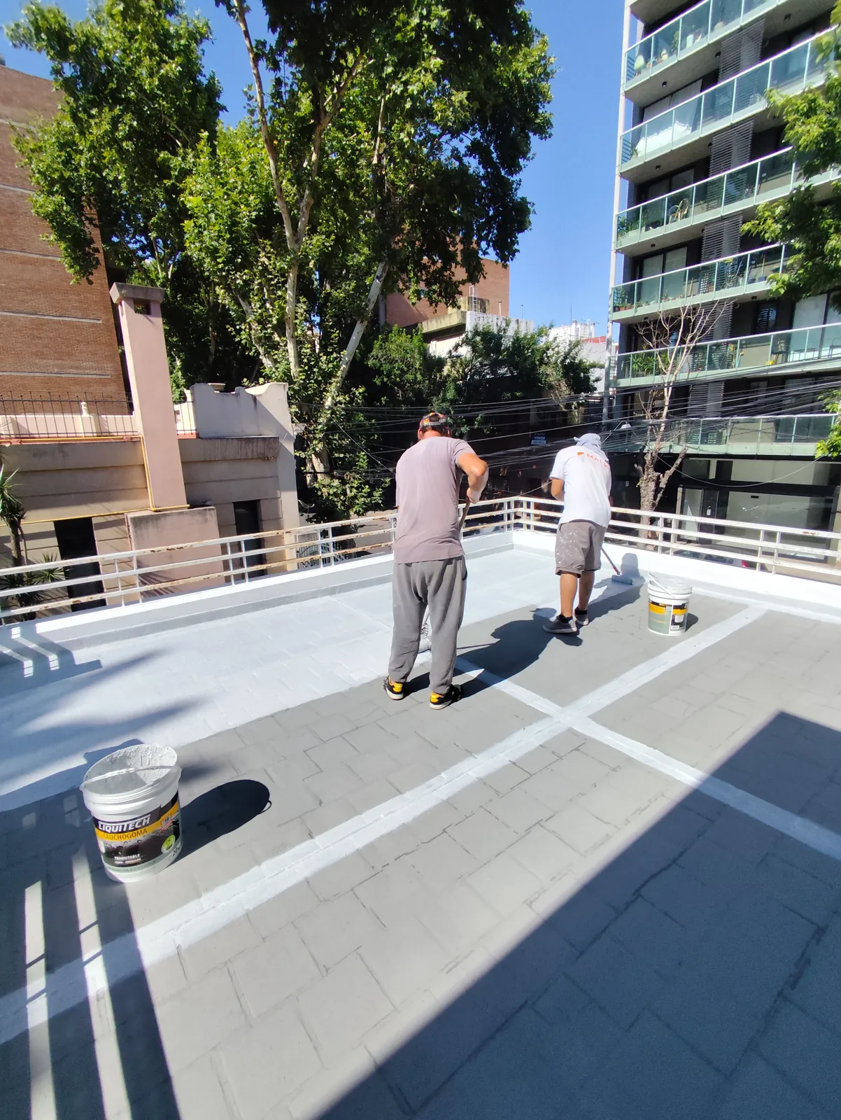 Operarios aplicando membrana en la terraza de un edificio.