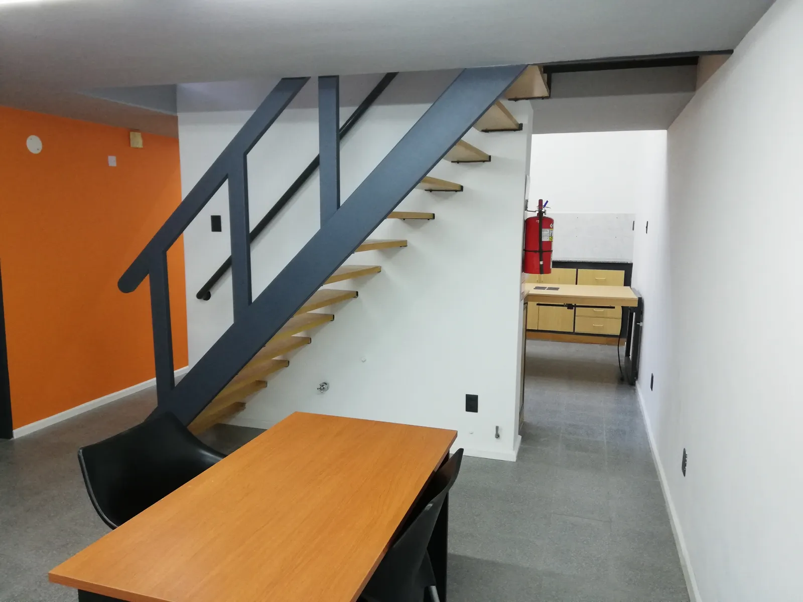 Oficina con pared naranja y escalera metálica.