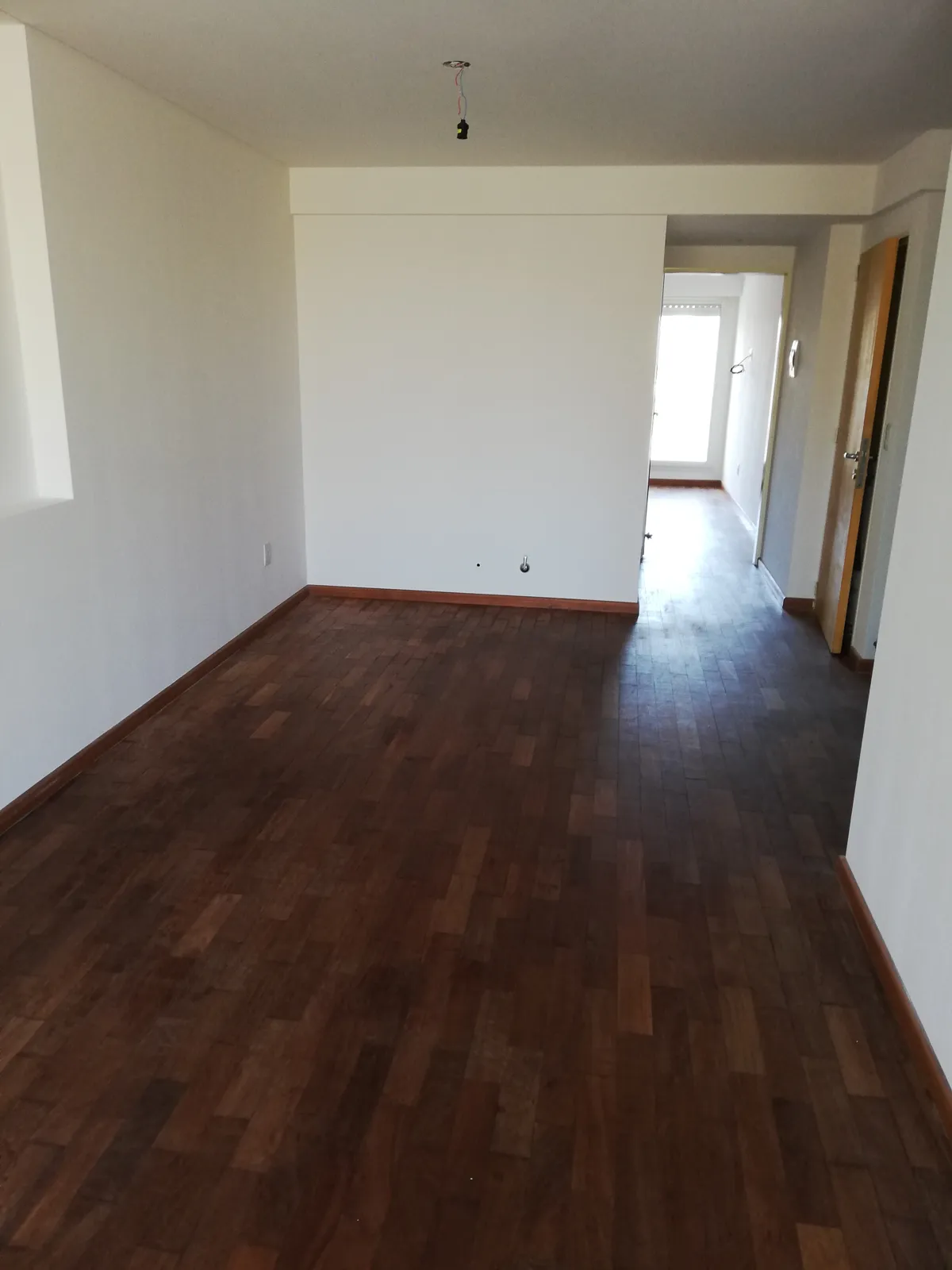 Ambiente de departamento pintado de blanco, piso de madera.