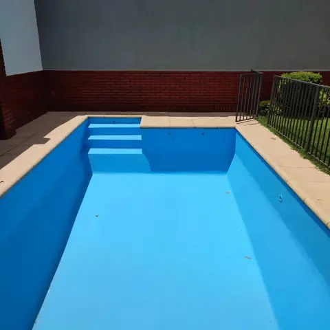 La misma pileta pintada de celeste, con pared de ladrillo al fondo.