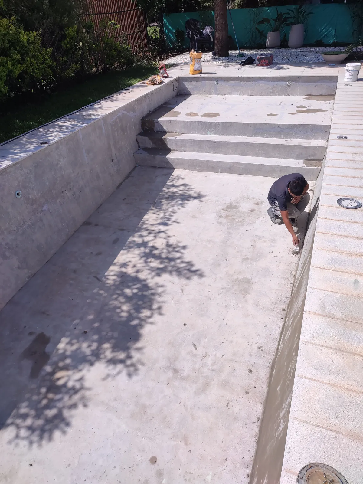 Operario trabajando en el revestimiento de una pileta con escalera.