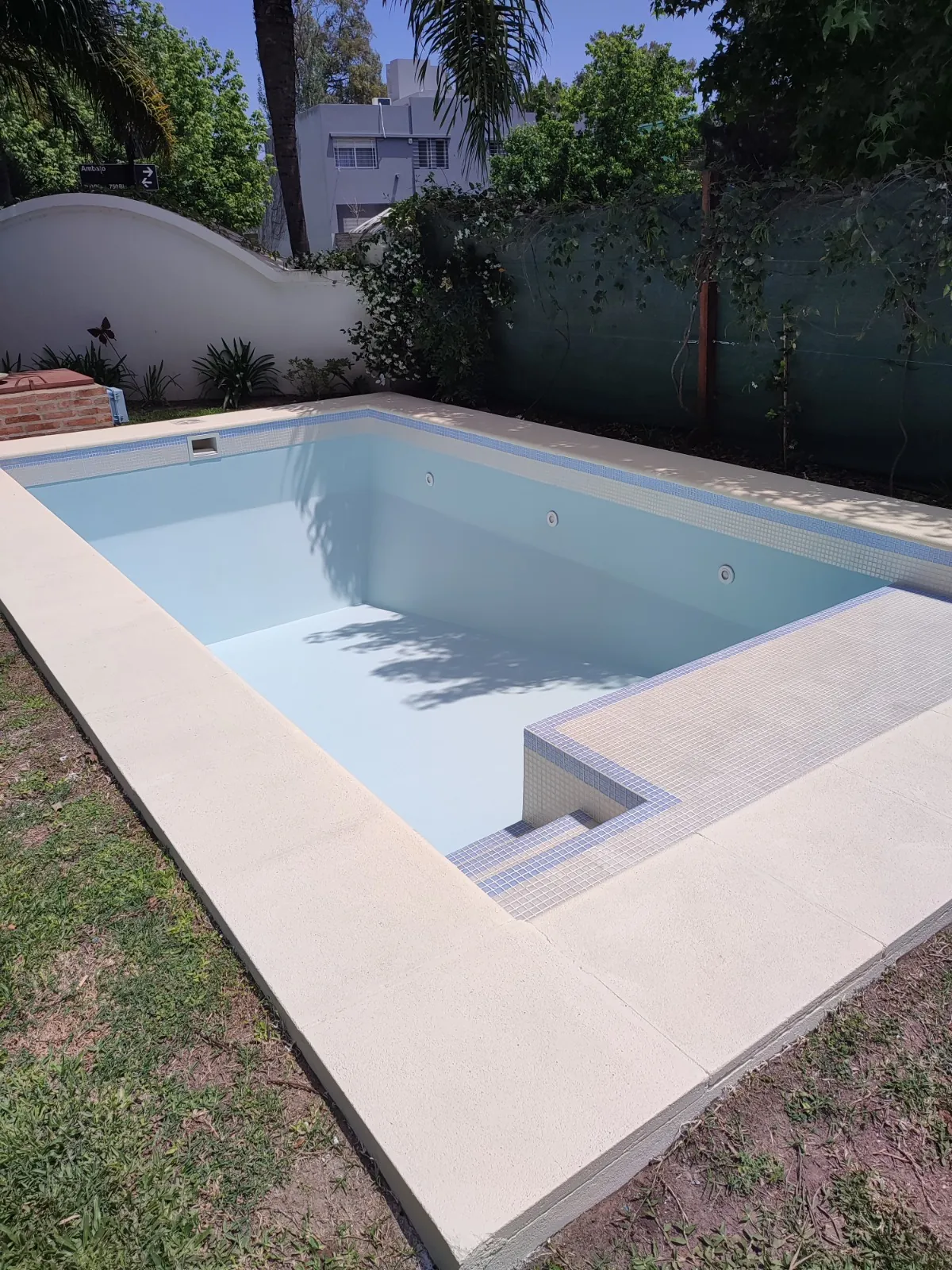 Pileta terminada en un jardín, con borde de piedra clara.