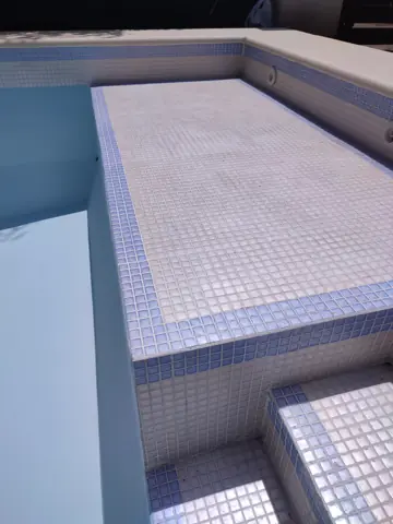 Banco de la pileta terminado con venecitas claras y borde azul.