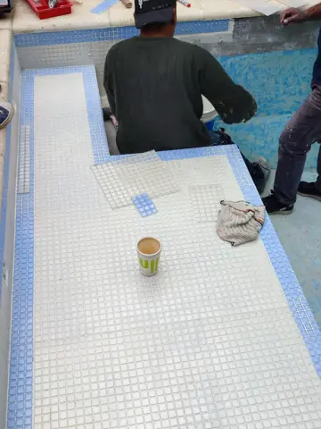 Operario colocando venecitas en el banco de una pileta.