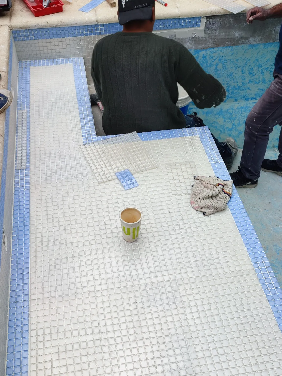 Operario colocando venecitas en el banco de una pileta.