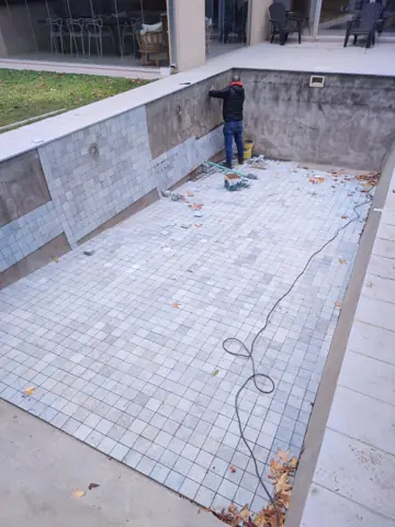 Pileta con venecitas en obra, con un operario en el fondo.